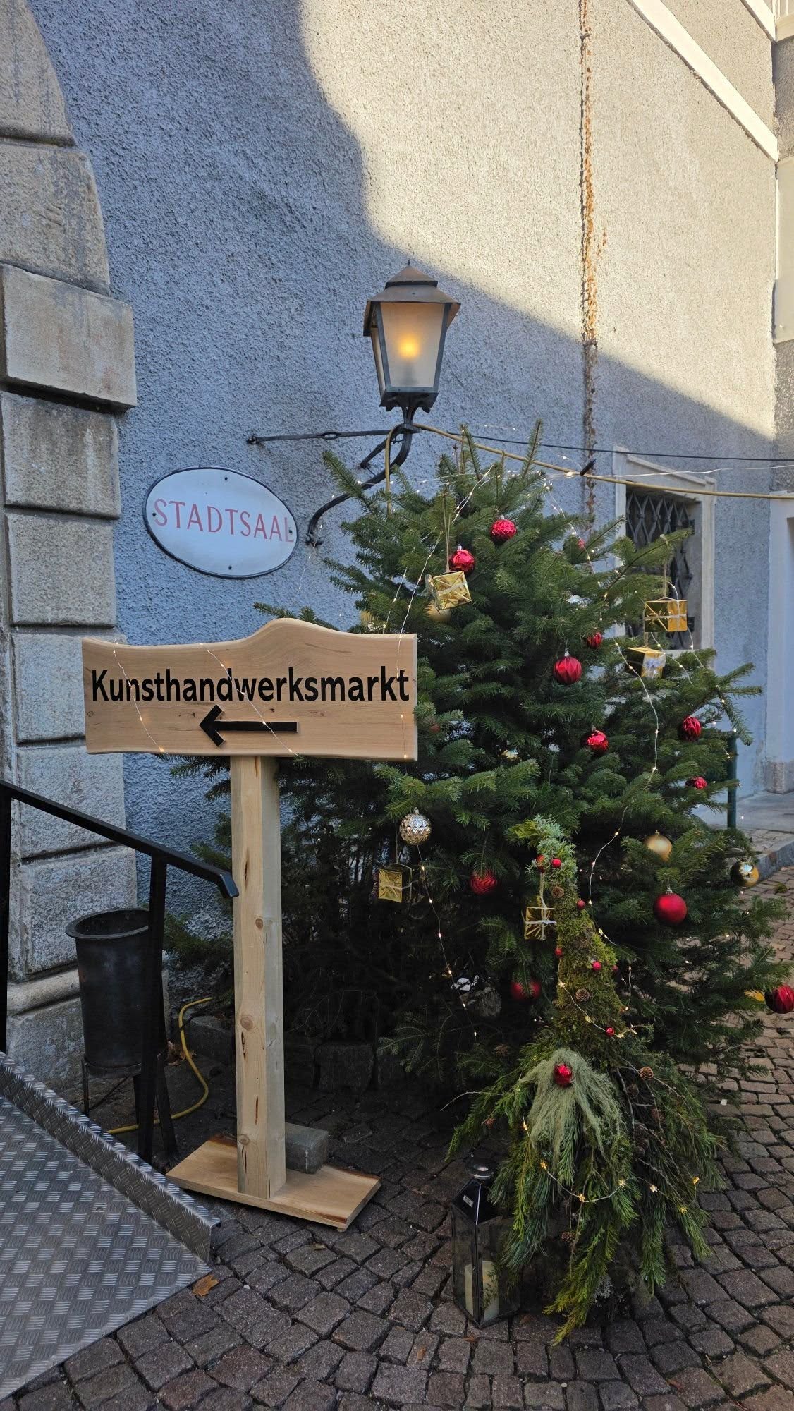Ez egy Kézműves Vásár (Kunsthandwerksmarkt) tábla egy karácsonyfával díszített, osztrák épület mellett. - Z(s)eppelin utazás